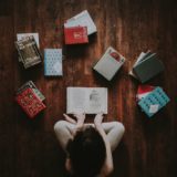 flat lay photography of woman sitting on brown wooden parquet flooring surrounded by books